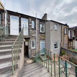 Stone row houses with concrete stairs and green iron railings on a sloped street under a cloudy sky