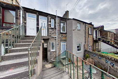 Stone row houses with concrete stairs and green iron railings on a sloped street under a cloudy sky