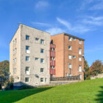 Two-tone residential building with beige and orange façades under a clear blue sky, grassy foreground below