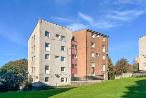 Two-tone residential building with beige and orange façades under a clear blue sky, grassy foreground below